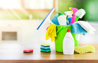 Cleaning items in green plastiv bucket on wooden table in new modern kitchen. Yellow gloves,...