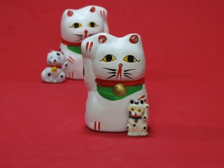 Four little Maneki Neko, Japanese lucky cats, amulets. Two cats in the foreground, that look like father (mother) and son, are well focused. The others, behind, are out of focus. Red background.