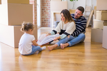 Beautiful family sitting on the floor playing with his kid at new home around cardboard boxes