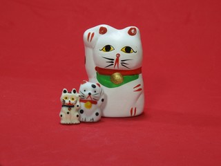 Three little Maneki Neko, Japanese lucky cats, amulets that bring good luck, protection, prosperity, health and happiness. They look like father (mother) and sons. Red background.