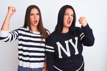 Young beautiful women wearing casual clothes standing over isolated white background angry and mad raising fist frustrated and furious while shouting with anger. Rage and aggressive concept.