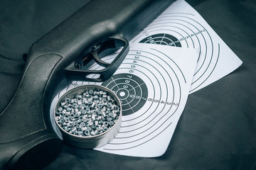 Air rifle, cartridges and paper target on a black background, top view