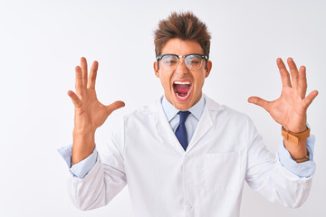 Young handsome sciencist man wearing glasses and coat over isolated white background celebrating mad and crazy for success with arms raised and closed eyes screaming excited. Winner concept