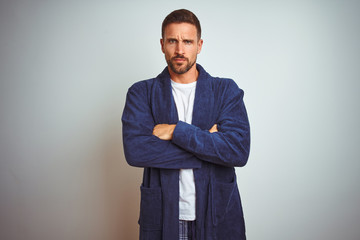 Young man wearing comfortable pajamas and robe at morning over isolated background skeptic and...