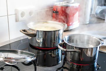Hausfrau kocht Nudeln und Wasser für das Mittagessen mit der Familie in silbernen Töpfen auf Induktionsherd mit heißen Kochfeldern als leckeres Mahl