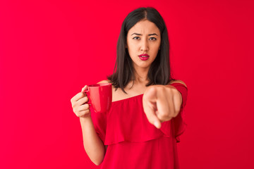 Young beautiful chinese woman drinking cup of coffee standing over isolated red background pointing with finger to the camera and to you, hand sign, positive and confident gesture from the front
