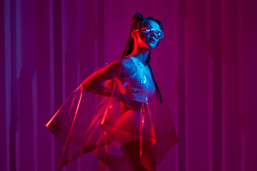 Cyberpunk and neon, a young trend girl in a transparent latex raincoat.