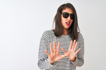 Chinese woman wearing striped t-shirt and sunglasses standing over isolated white background afraid and terrified with fear expression stop gesture with hands, shouting in shock. Panic concept.