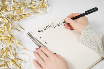 Female hands writing My Goals 2020 in a notebook. Tinsel, New Years concept