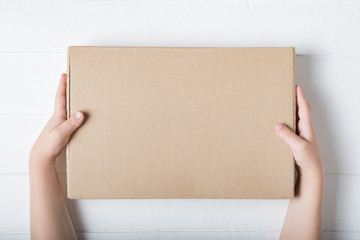 Rectangular cardboard box in children's hands. Top view, white background - obrazy, fototapety, plakaty