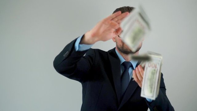 Formally dressed man scatters dollar bills around him, making money rain