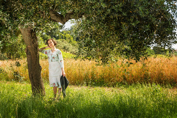 Woman in 40's clothes under an olive tree in the Abruzzo countryside with a field of wheat in the background