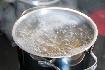 Mittagessen im dampfenden Kochtopf wird auf heißer Herdplatte in der Küche von einer Hausfrau für die Familie gekocht und zubereitet mit Verletzungsgefahr und Verbrennungsgefahr