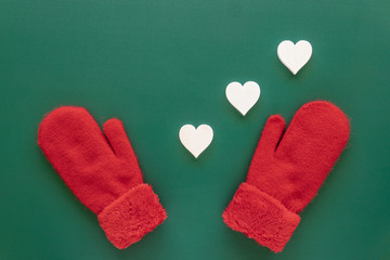Red knitted mittens and decorative white hearts on a green background.