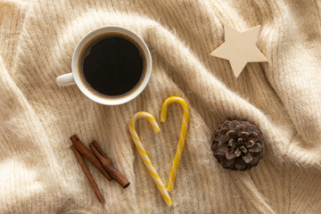Christmas candies laid out in the shape of heart, cup of coffee, pine cone, cinnamon sticks on a warm knit wool plaid. Winter, New Year, Christmas background. Top view.