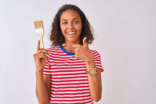 Young brazilian painter woman holding brush standing over isolated white background very happy pointing with hand and finger