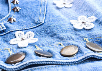Fototapeta na wymiar Denim Fabric pattern blue Jeans old ripped torn vintage fashion design decoration by white flowers and buttons background Jean texture closeup soft focus.