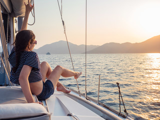 attractive young woman in a striped t-shirt enjoys the sunset on the deck of a sailing yacht. Sailing regatta