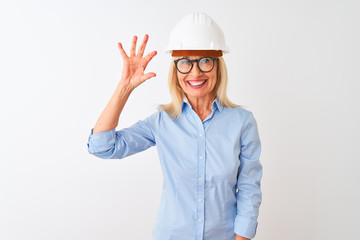 Middle age architect woman wearing glasses and helmet over isolated white background smiling and confident gesturing with hand doing small size sign with fingers looking and the camera. 