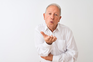 Senior grey-haired man wearing elegant shirt standing over isolated white background looking at the camera blowing a kiss with hand on air being lovely and sexy. Love expression.