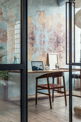 Stylish interior design of office space in loft apartment with wooden desk, chair, office supplies, laptop, plants and elegant accessories. Modern home office decor. Bright space. Template.