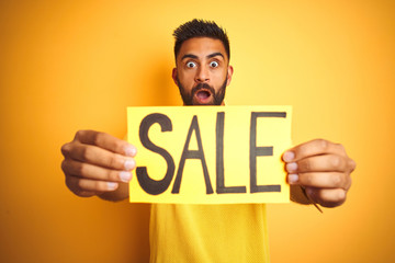 Young arab indian hispanic man holding sale banner over isolated yellow background scared in shock with a surprise face, afraid and excited with fear expression