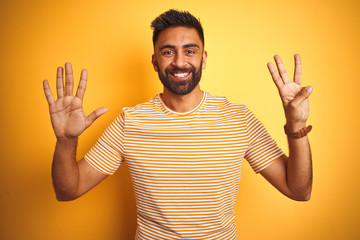 Young indian man wearing t-shirt standing over isolated yellow background showing and pointing up with fingers number eight while smiling confident and happy.