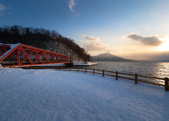 scenic view at Yamasentetsu Bridge in winter at sunset time with view of trees without leaves at Lake Shikotsu, Chitose, Hokkaido, Japan