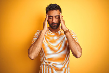 Young indian man wearing t-shirt standing over isolated yellow background with hand on headache because stress. Suffering migraine.