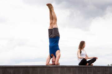 man stands on the head and woman sits in meditation yoga pose - relationship concept