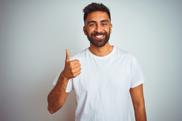 Young indian man wearing t-shirt standing over isolated white background doing happy thumbs up...