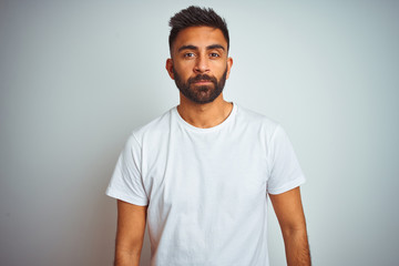 Young indian man wearing t-shirt standing over isolated white background Relaxed with serious expression on face. Simple and natural looking at the camera.
