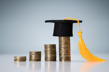 Graduation Hat On Top Of Coin Stack Over Desk