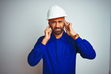 Handsome indian worker man wearing uniform and helmet over isolated white background covering ears...