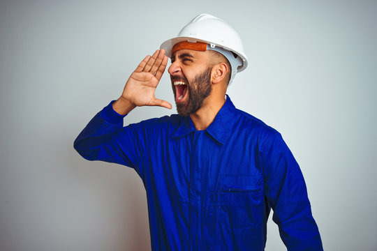 Handsome indian worker man wearing uniform and helmet over isolated white background shouting and screaming loud to side with hand on mouth. Communication concept.