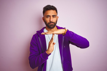 Young indian man wearing purple sweatshirt standing over isolated pink background Doing time out...