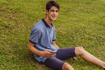 Young teenage boy sitting in park using mobile phone.