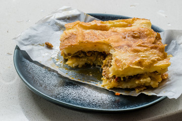 Bitten Turkish Borek with Minced Meat and Leek on Wooden Board / Burek leftover.
