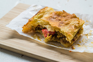 Bitten Turkish Borek with Minced Meat and Leek on Wooden Board / Burek leftover.