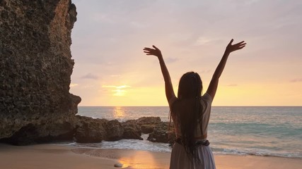 happy woman stand on sand of the sea and show hand in to sky. subject is blurred. Woman expressing joy in cave beside the sea.
