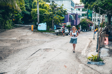 Elderly senior Asian traveling backpacker mature woman tourist walking enjoying taking photos in Sanya local street outdoor. Traveling along Asia, active lifestyle concept. Discovering Hainan, China