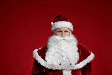 Portrait of senior man wearing Santa costume with white beard looking at camera isolated on red background