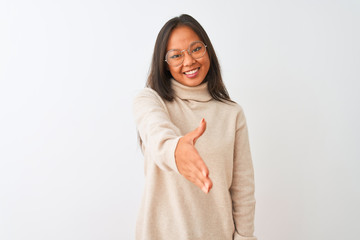 Fototapeta premium Young chinese woman wearing turtleneck sweater and glasses over isolated white background smiling friendly offering handshake as greeting and welcoming. Successful business.