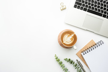 White office desk table with blank notebook, pen, laptop computer, cup of latte coffee and...