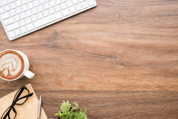 Wood office desk table with computer keyboard, cup of latte coffee and supplies. Top view with copy...