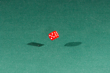 One red dice falling on a green table