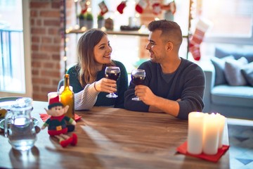 Young beautiful couple smiling happy and confident. Toasting with cup of wine celebrating christmas at home