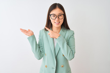 Chinese businesswoman wearing elegant jacket and glasses over isolated white background amazed and smiling to the camera while presenting with hand and pointing with finger.