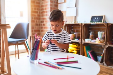 Beautiful toddler boy drawing cute draw using colored pencils at kindergarten