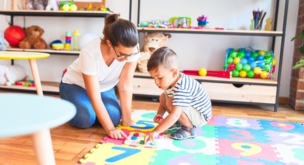 Fototapeta premium Beautiful teacher and toddler boy sitting on puzzle playing with numbers at kindergarten